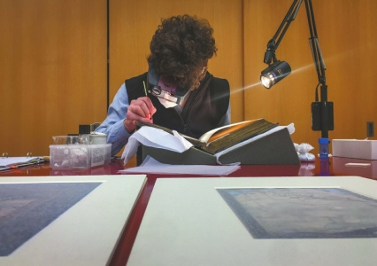 一名修復(fù)師正在聚光燈下修復(fù)一本印度的古書。