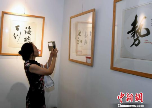 一名女性觀眾用手機(jī)拍攝參展書法作品?！∮浾邉⒖筛?攝