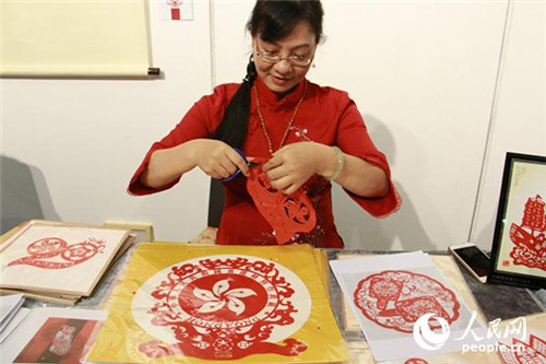 潮陽(yáng)剪紙傳承人魏惠君現(xiàn)場(chǎng)展示，她的面前就擺放著專為此次展覽設(shè)計(jì)的“20”(左一)和區(qū)徽(左二)圖樣。(攝影：吳玉潔)