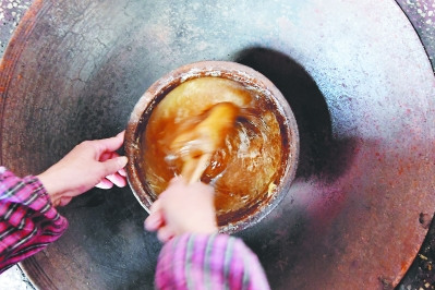 熬制糖汁需要土灶恒溫，林傳星的妻子孫巧瑤要守在旁邊片刻不停地攪拌翻動，直至呈深褐色的膠狀。