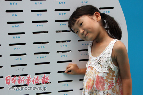 一名日本兒童正向?qū)懹凶约好值耐稁趴诶锓湃?00日元。(日本新華僑報網(wǎng))